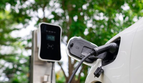 Focus closeup electric vehicle plugged in with EV charger device from blurred background of public charging station powered by renewable clean energy for progressive eco-friendly car concept.